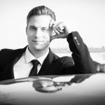 portrait d un homme en noir et blanc appuyé sur une voiture